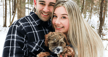The cutest chocolate Havapoo puppy walking through a field of flowers.