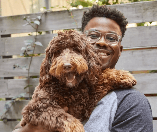 Young man smiling and hugging a brown puppy while standing