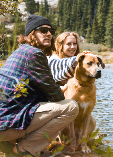 Man and woman sitting with their dog by a river in nature