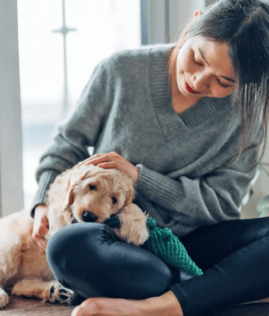 Lady sitting and petting a puppy who is leaning on her foot